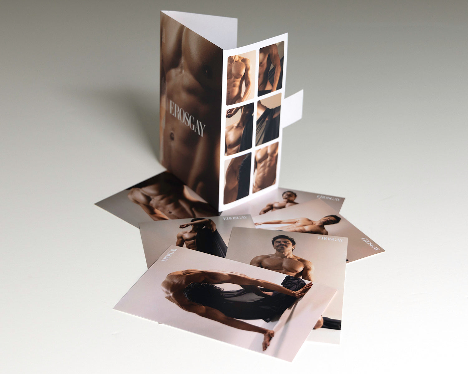 Sixpack de Mauricio de ErosGay con el contenido afuera: el sobre/estuche abierto a un lado y seis impresiones extendidas sobre una superficie clara, con sombras suaves.
