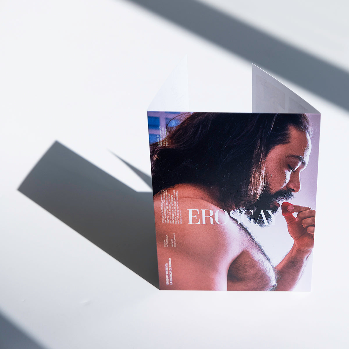 Empaque del Sixpack de Arturo de ErosGay, en vista frontal; portada a color con retrato de perfil de un hombre de cabello largo sosteniendo un pétalo rojo cerca de la boca, con el logotipo “EROSGAY” centrado.