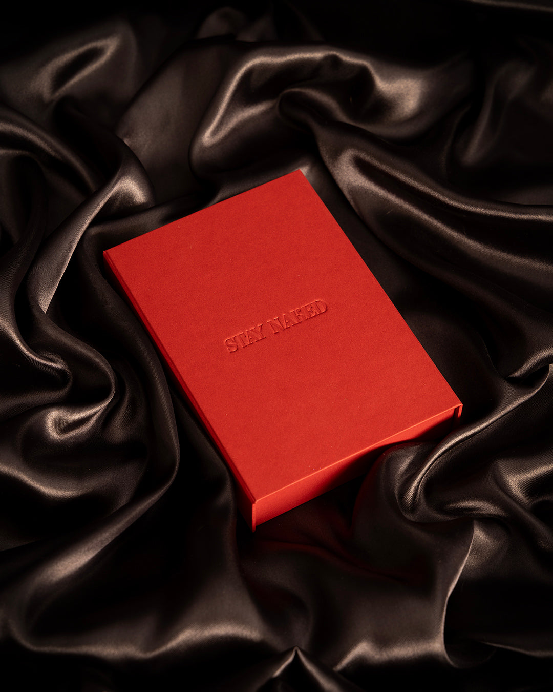 caja de color rojo con grabado dque dice stay naked cobre fondo de tela satinada de color negro