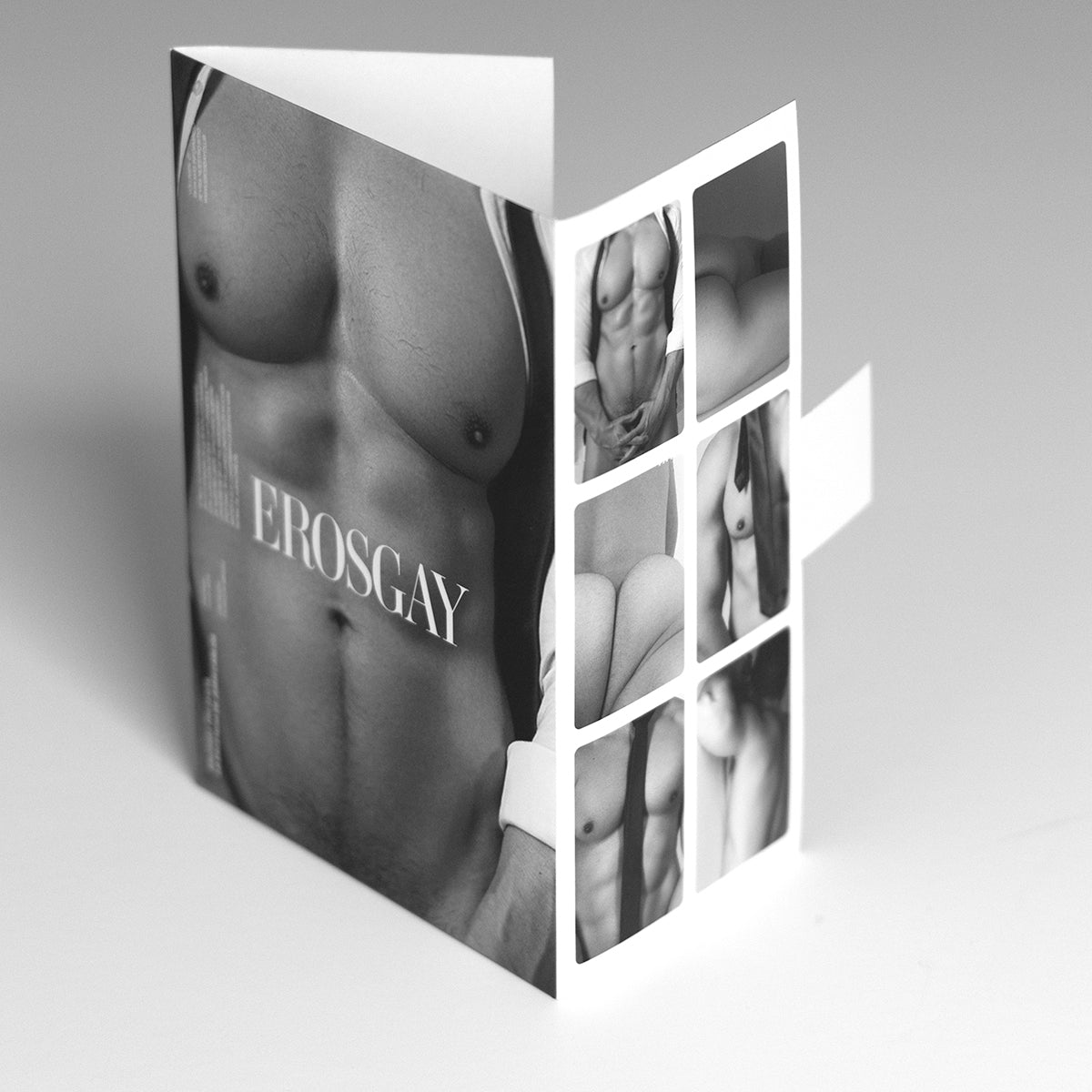 Sixpack de ErosGay del modelo Juan en empaque tipo sobre desplegable, fotografiado en blanco y negro sobre fondo claro. Al frente se ve un close-up del torso masculino con el logotipo ‘EROSGAY’ al centro; en la solapa interior aparecen seis miniaturas de la colección en una cuadrícula