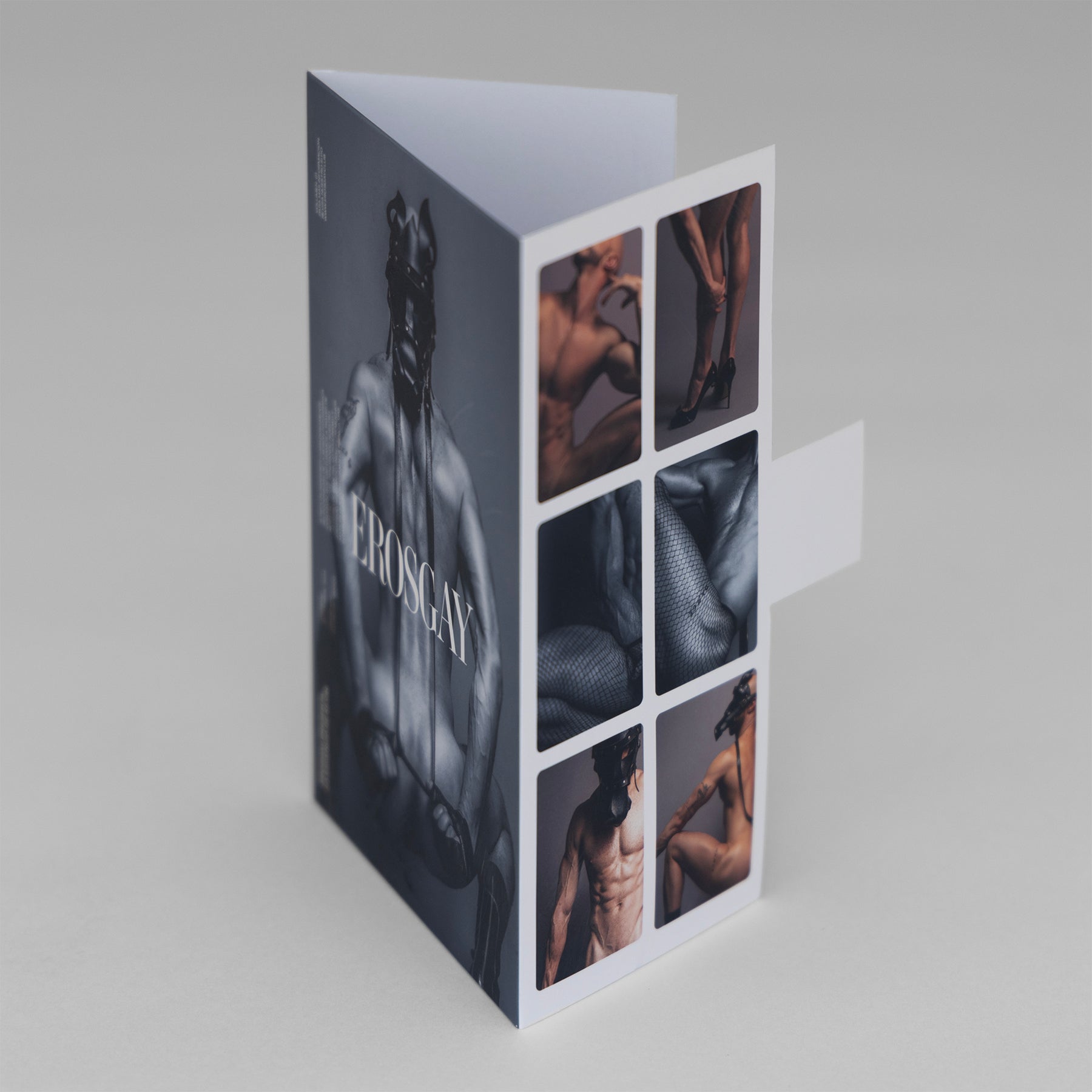 Vista lateral del sobre del sixpack de Kevin (ErosGay) sobre fondo gris. Se aprecia el lomo y parte de la portada en blanco y negro con el logo ‘EROSGAY’ en vertical, mientras que el panel trasero muestra una retícula de seis miniaturas a color (detalles de cuerpo, textura de malla y poses parciales). La lengüeta de cierre blanca sobresale hacia la derecha y las solapas superiores quedan ligeramente abiertas