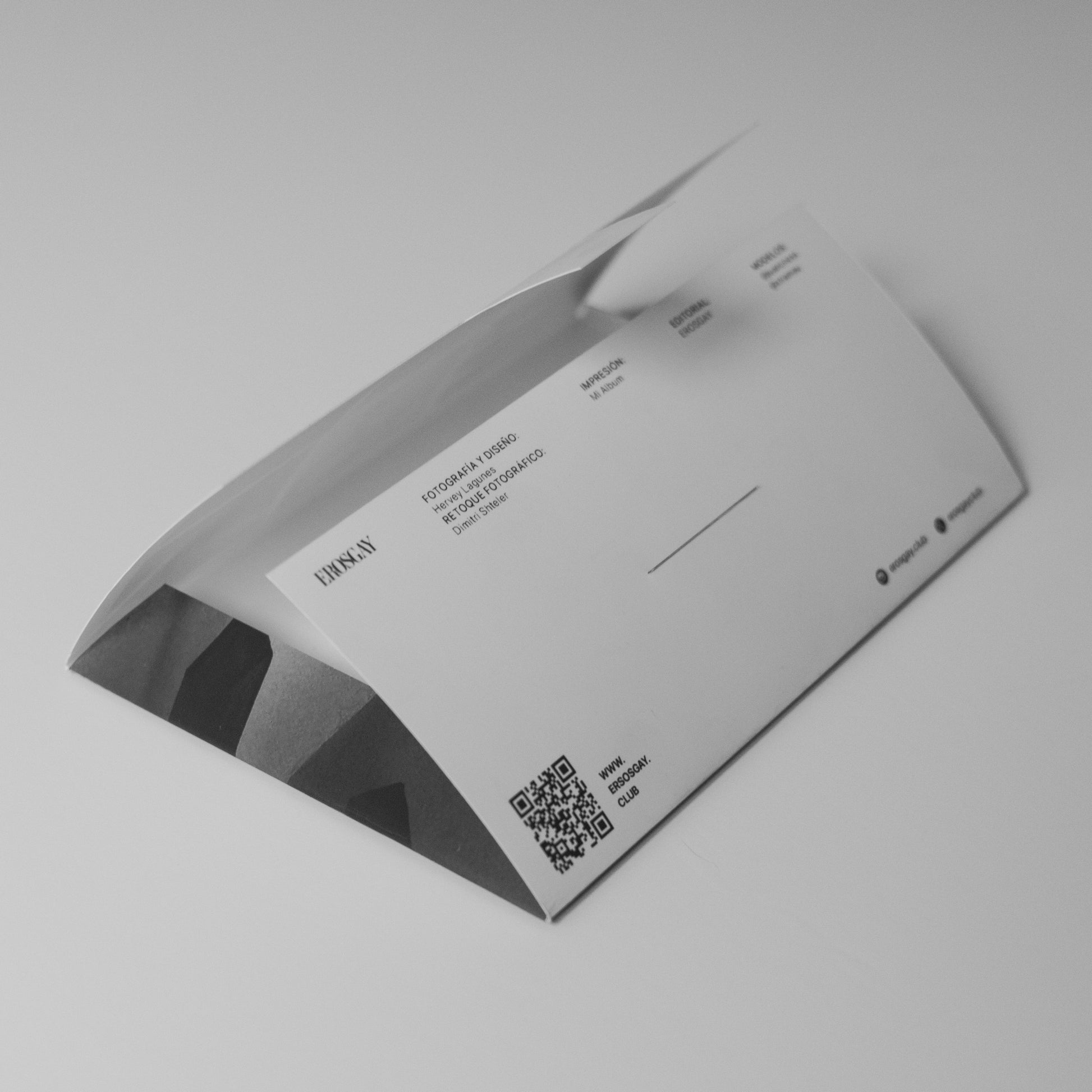 Parte trasera del Sixpack de Mauricio y Juan de ErosGay: sobre abierto en blanco y negro con créditos impresos, redes sociales y un código QR, fotografiado sobre fondo claro.