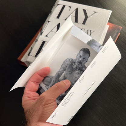 Sixpack de José de ErosGay abierto en una mano; se ve una impresión en blanco y negro dentro del sobre, con los créditos impresos en el lateral, sobre una mesa oscura.