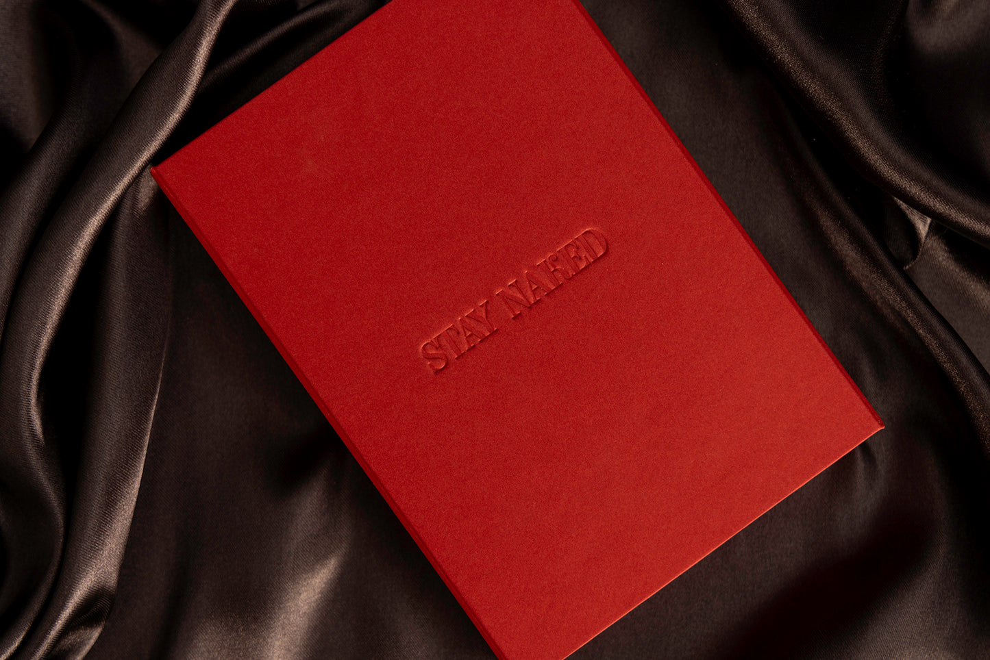 caja de color rojo con grabado dque dice stay naked cobre fondo de tela satinada de color negro